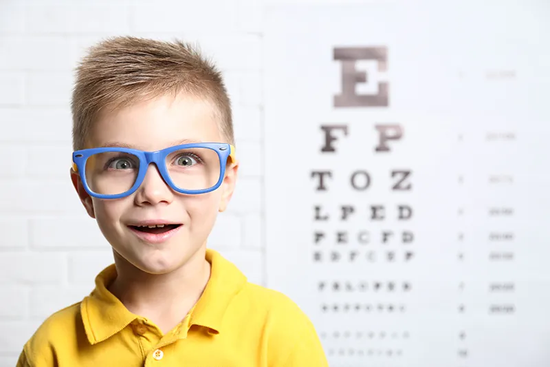Young boy wearing glasses in front of an eye chart